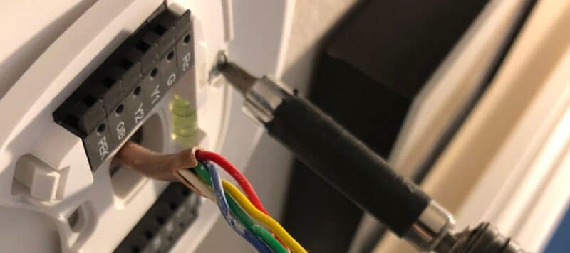 Close-up of a thermostat wiring installation with a screwdriver