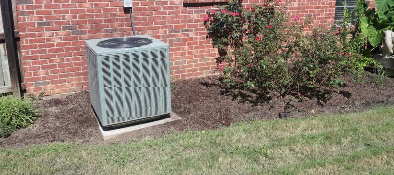 outdoor hvac unit positioned outside of a red brick home surrounded by green grass and shubbery